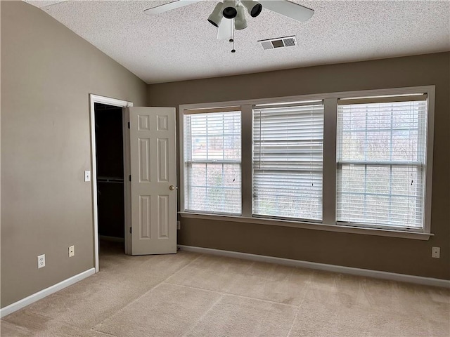 spare room with light carpet, baseboards, visible vents, vaulted ceiling, and a textured ceiling