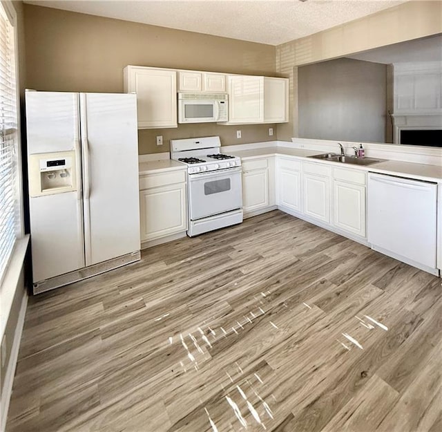 kitchen with white appliances, white cabinetry, a sink, and light wood-style flooring