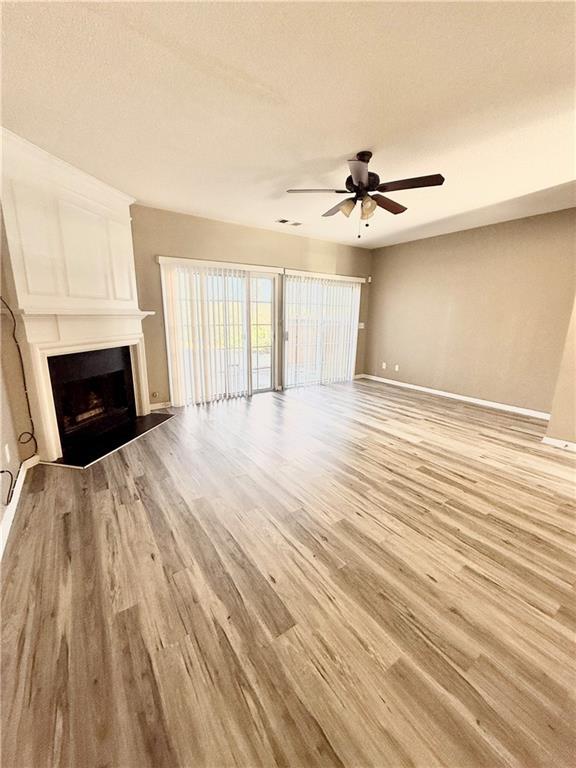 unfurnished living room featuring light wood-type flooring, a large fireplace, ceiling fan, and baseboards