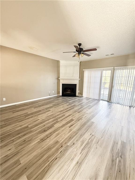 unfurnished living room featuring a large fireplace, baseboards, visible vents, a ceiling fan, and light wood-type flooring