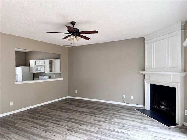 unfurnished living room featuring a large fireplace, ceiling fan, baseboards, and wood finished floors