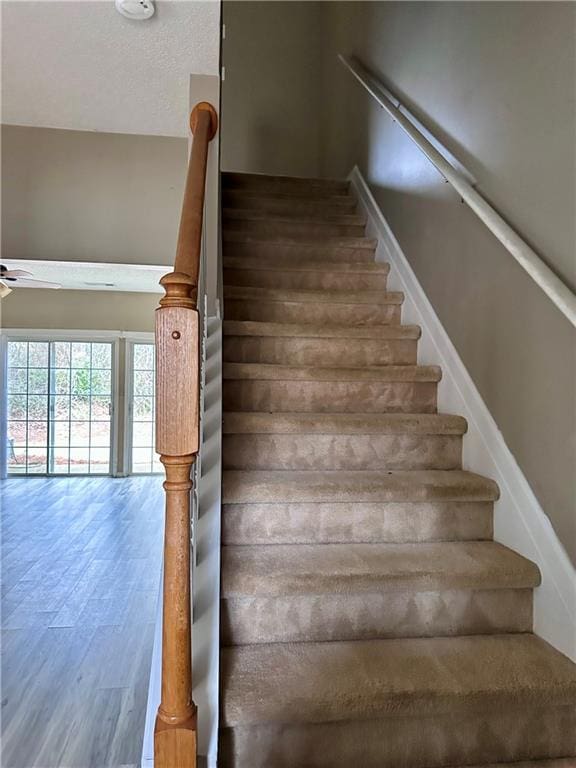 stairs with ceiling fan, a textured ceiling, and wood finished floors