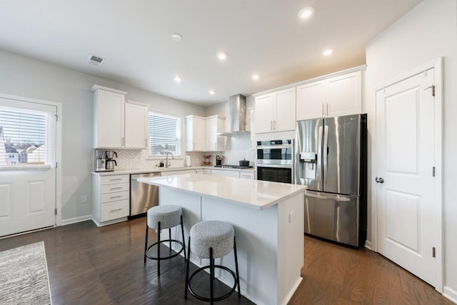 kitchen with tasteful backsplash, wall chimney exhaust hood, stainless steel appliances, light countertops, and a kitchen bar