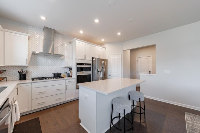 kitchen with tasteful backsplash, white cabinets, wall chimney exhaust hood, a breakfast bar, and stainless steel appliances