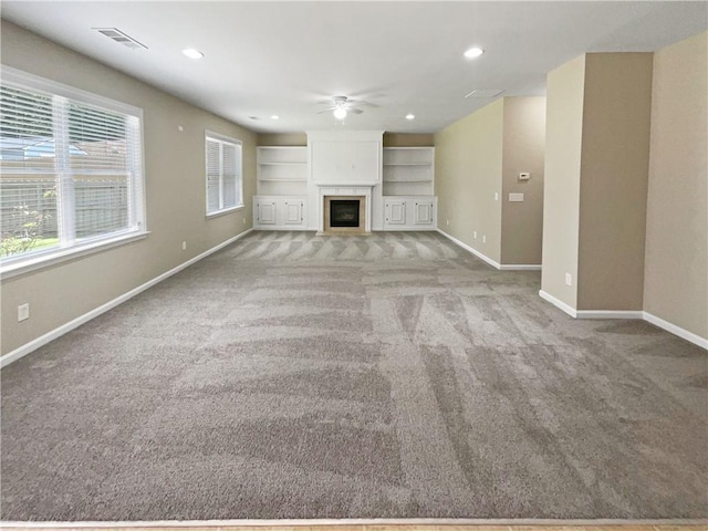 unfurnished living room with ceiling fan, built in shelves, and light colored carpet