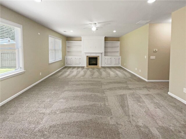 unfurnished living room with built in shelves, light colored carpet, and ceiling fan