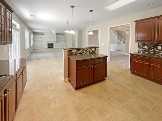 kitchen with decorative light fixtures, light carpet, tasteful backsplash, and dark stone counters