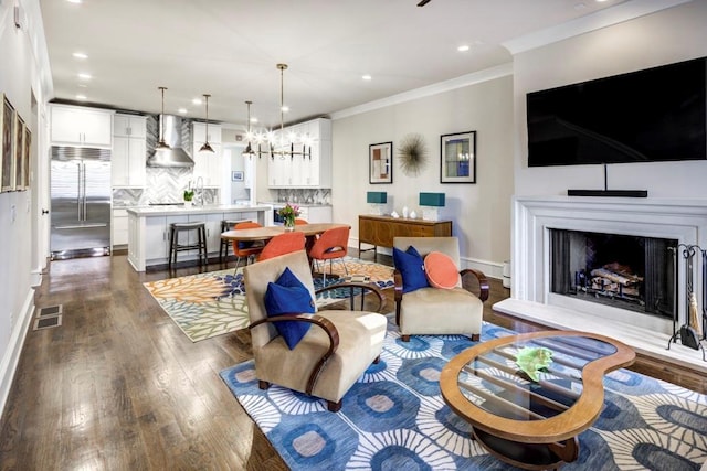 living area with dark wood-type flooring, crown molding, a fireplace with raised hearth, recessed lighting, and baseboards