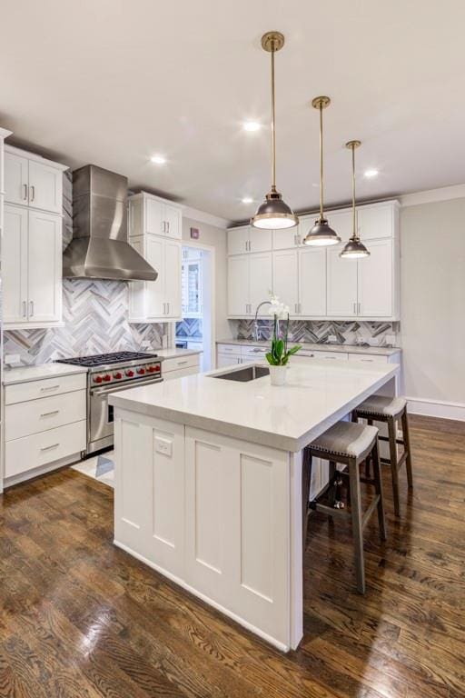 kitchen with wall chimney range hood, high end stove, backsplash, a center island with sink, and crown molding