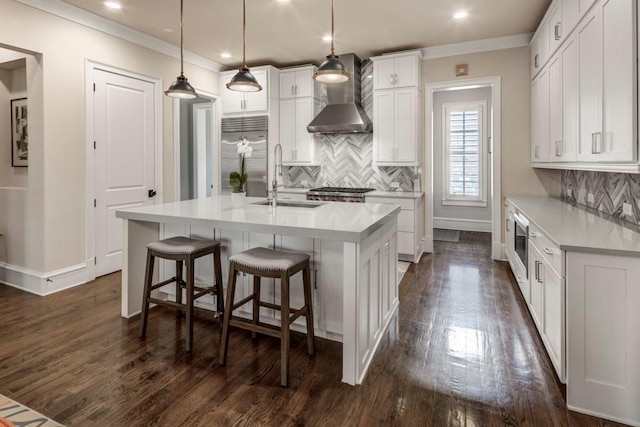 kitchen with wall chimney range hood, built in refrigerator, a sink, decorative backsplash, and white cabinets