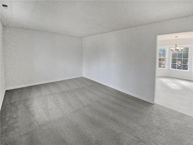 unfurnished room with a textured ceiling, carpet flooring, and a chandelier