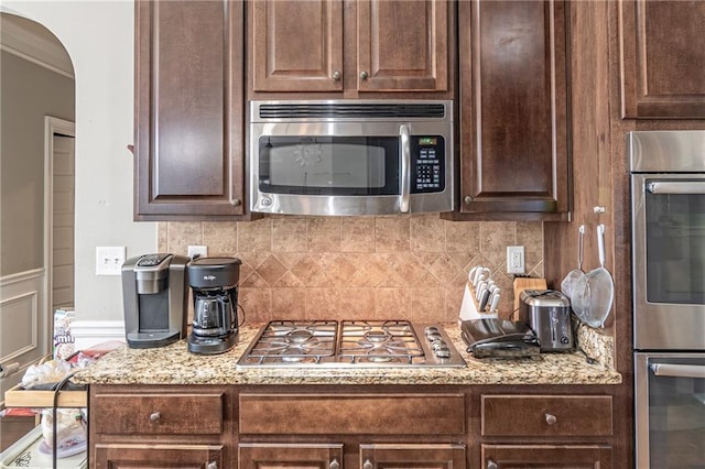 2183 Trinity Grove Ct, Dacula, GA 30019 - kitchen featuring appliances with stainless steel finishes, dark brown cabinets, arched walkways, tasteful backsplash, and ornamental molding