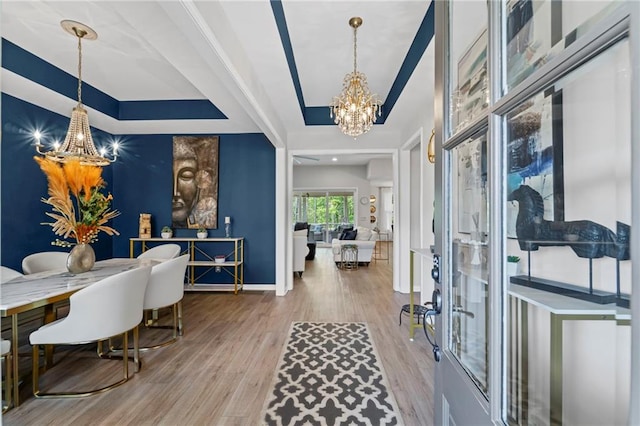 entrance foyer with a chandelier, wood finished floors, a raised ceiling, and baseboards