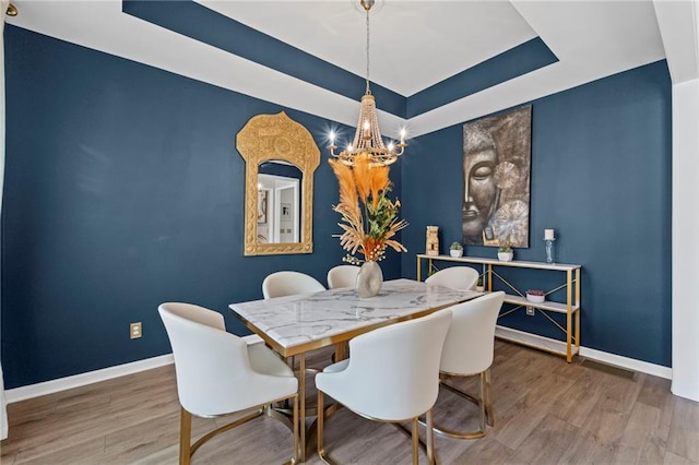 dining space featuring baseboards, a chandelier, wood finished floors, and a raised ceiling