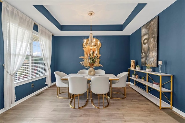 dining room with a chandelier, a raised ceiling, baseboards, and wood finished floors