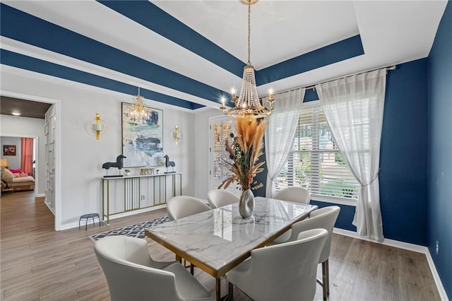 dining room featuring a chandelier, baseboards, a raised ceiling, and wood finished floors