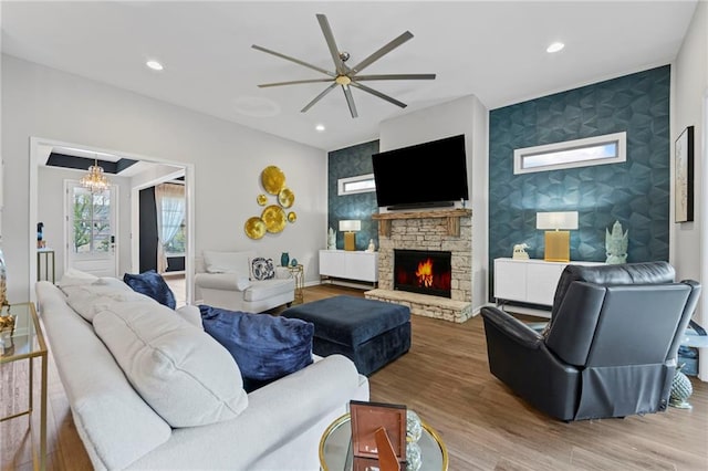 living area featuring an accent wall, ceiling fan, a stone fireplace, wood finished floors, and recessed lighting