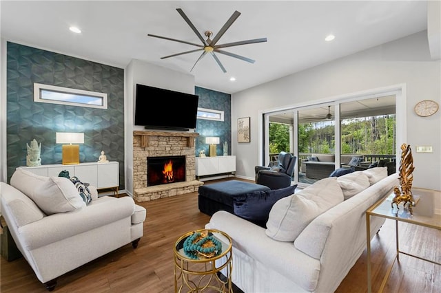 living area featuring an accent wall, ceiling fan, a fireplace, wood finished floors, and recessed lighting