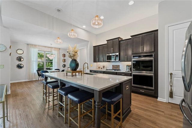 kitchen with appliances with stainless steel finishes, a sink, a kitchen breakfast bar, dark brown cabinetry, and wood finished floors