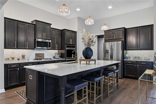 kitchen featuring appliances with stainless steel finishes, a sink, decorative backsplash, a chandelier, and a breakfast bar