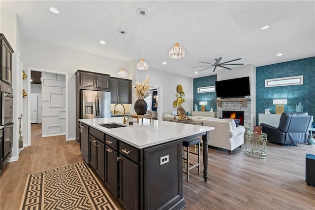 kitchen with stainless steel appliances, a sink, a breakfast bar area, a ceiling fan, and wood finished floors