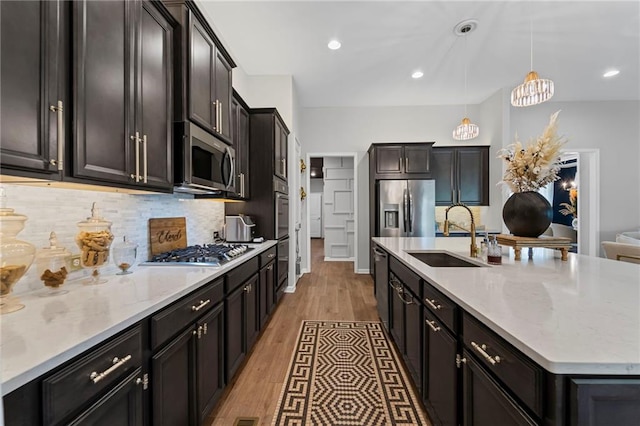 kitchen featuring a sink, appliances with stainless steel finishes, a large island, tasteful backsplash, and decorative light fixtures