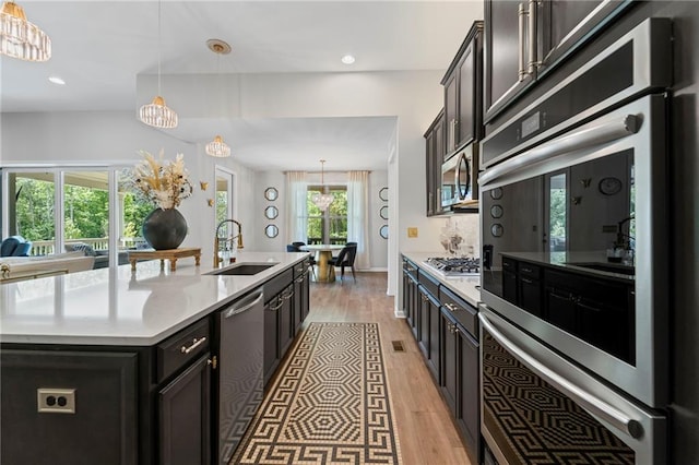 kitchen featuring a sink, appliances with stainless steel finishes, light wood-type flooring, a kitchen island with sink, and pendant lighting