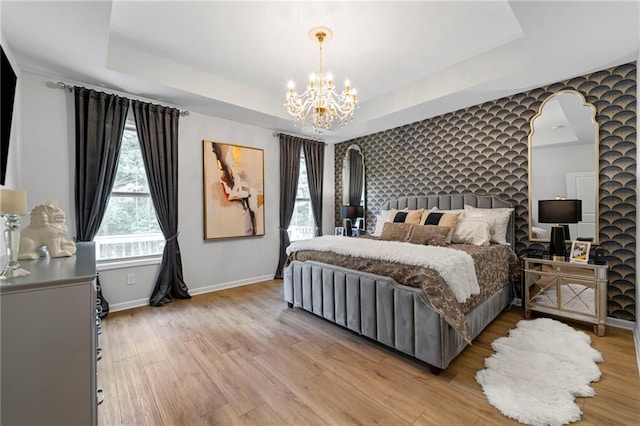 bedroom featuring a chandelier, light wood-style floors, a tray ceiling, and baseboards