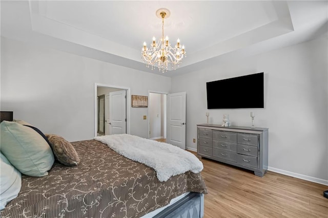 bedroom with a chandelier, a raised ceiling, baseboards, and wood finished floors
