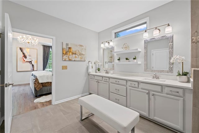 ensuite bathroom with healthy amount of natural light, double vanity, a chandelier, and baseboards