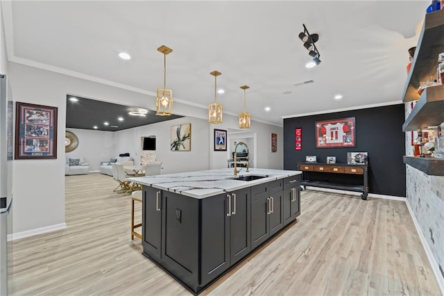 kitchen with a sink, light wood-style flooring, a center island with sink, crown molding, and pendant lighting
