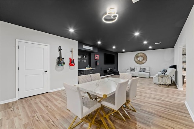 dining space featuring baseboards, light wood finished floors, recessed lighting, and bar