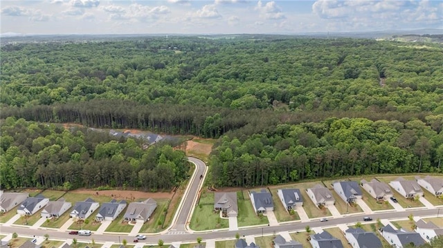 aerial view of property and surrounding area featuring a heavily wooded area and nearby suburban area