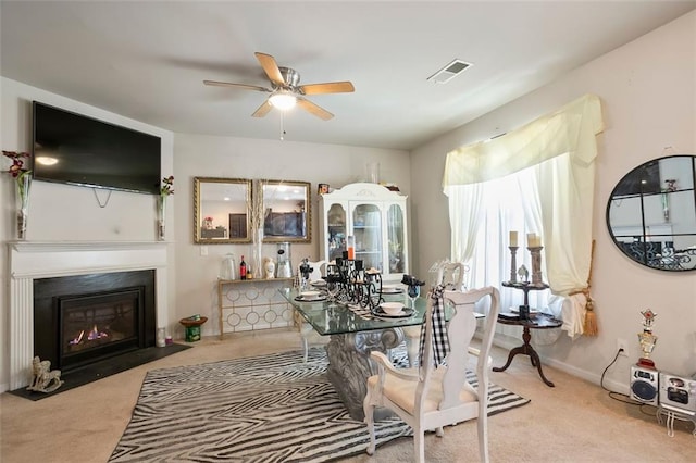 carpeted dining area with ceiling fan, visible vents, baseboards, and a fireplace with flush hearth