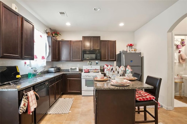 kitchen featuring a breakfast bar, a sink, visible vents, dark brown cabinets, and black appliances