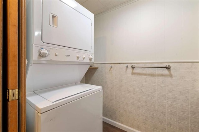 clothes washing area featuring stacked washing maching and dryer, tile walls, and ornamental molding