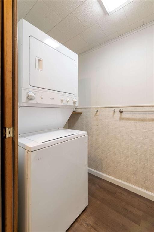 laundry room featuring stacked washer / drying machine, dark hardwood / wood-style floors, and tile walls