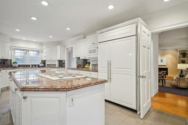 kitchen with light tile patterned flooring, white microwave, white cabinets, a kitchen island, and gas cooktop