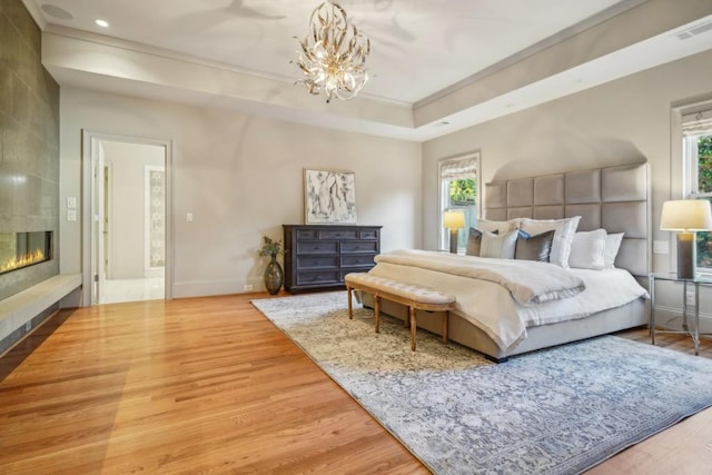 bedroom with a tile fireplace, a chandelier, hardwood / wood-style flooring, and a tray ceiling