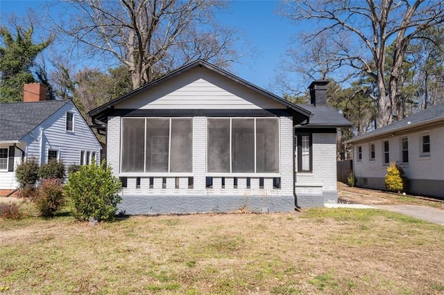 rear view of property with a sunroom, a chimney, a lawn, and brick siding