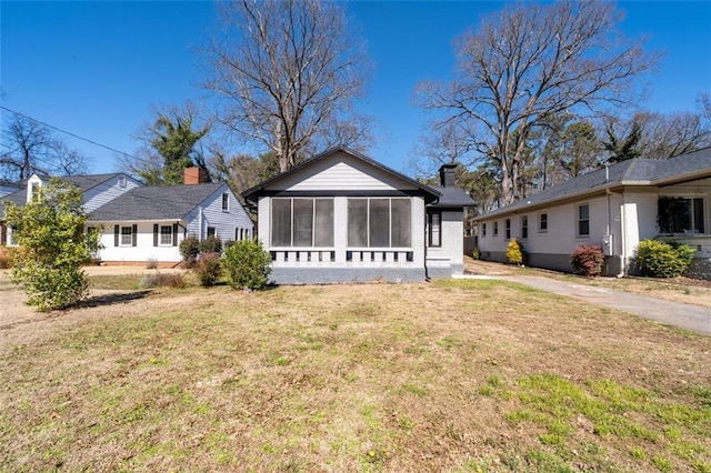 bungalow-style home featuring a sunroom, a chimney, and a front lawn