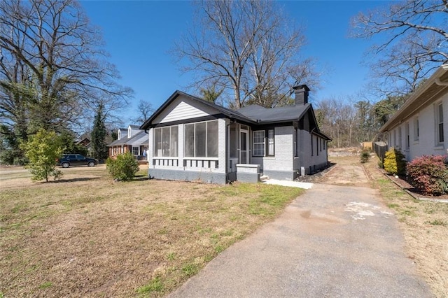 bungalow featuring brick siding, a chimney, a sunroom, driveway, and a front lawn