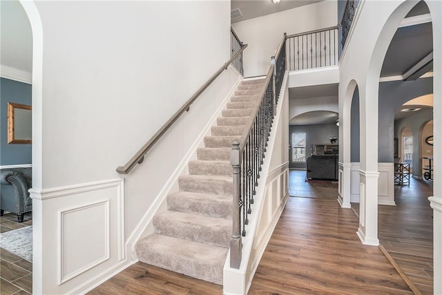 stairs with arched walkways, a wainscoted wall, wood finished floors, and a towering ceiling