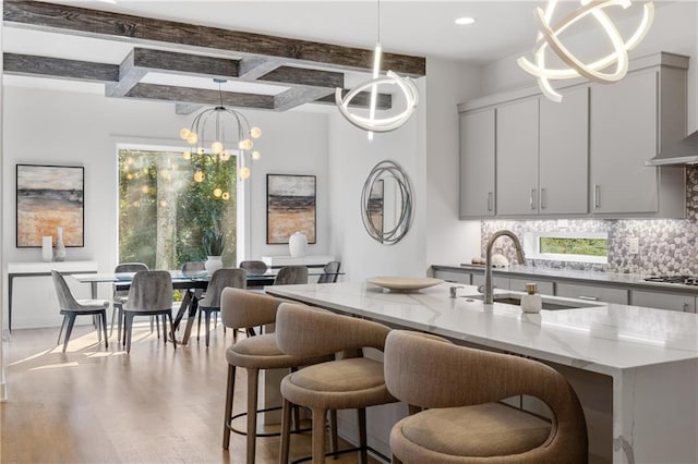 kitchen featuring beamed ceiling, tasteful backsplash, hanging light fixtures, a kitchen island with sink, and sink