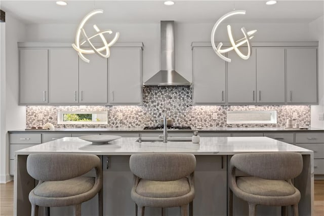 kitchen with light stone countertops, gray cabinetry, decorative light fixtures, an inviting chandelier, and wall chimney exhaust hood