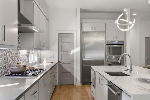 kitchen with white cabinets, wall chimney exhaust hood, stainless steel appliances, sink, and hanging light fixtures