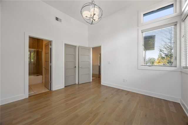 unfurnished bedroom featuring high vaulted ceiling, connected bathroom, a notable chandelier, and light wood-type flooring