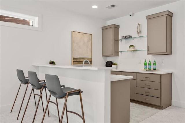 kitchen with kitchen peninsula, light colored carpet, a kitchen bar, and gray cabinets