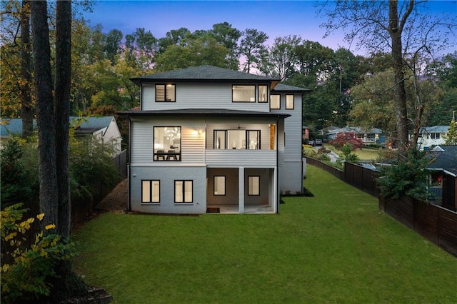 back house at dusk featuring a yard and a patio