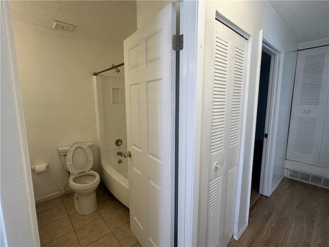 bathroom with a textured ceiling, hardwood / wood-style flooring, bathing tub / shower combination, and toilet